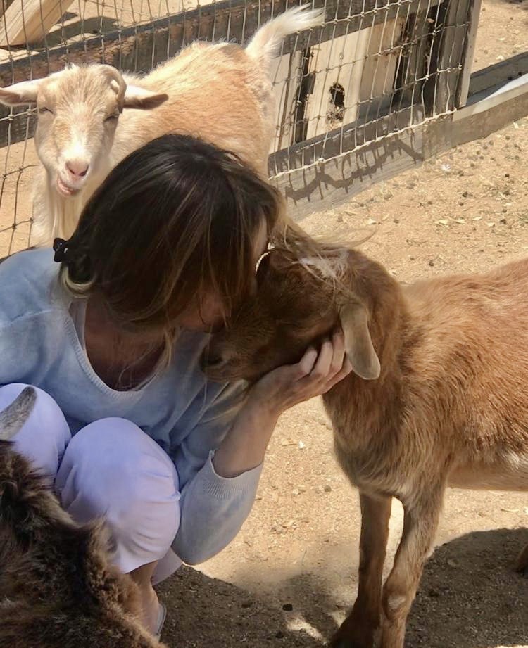 Woman gently nuzzling a goat outside a wooden barn — compassionate animal care in rural setting. about Southern California Pet Sitting