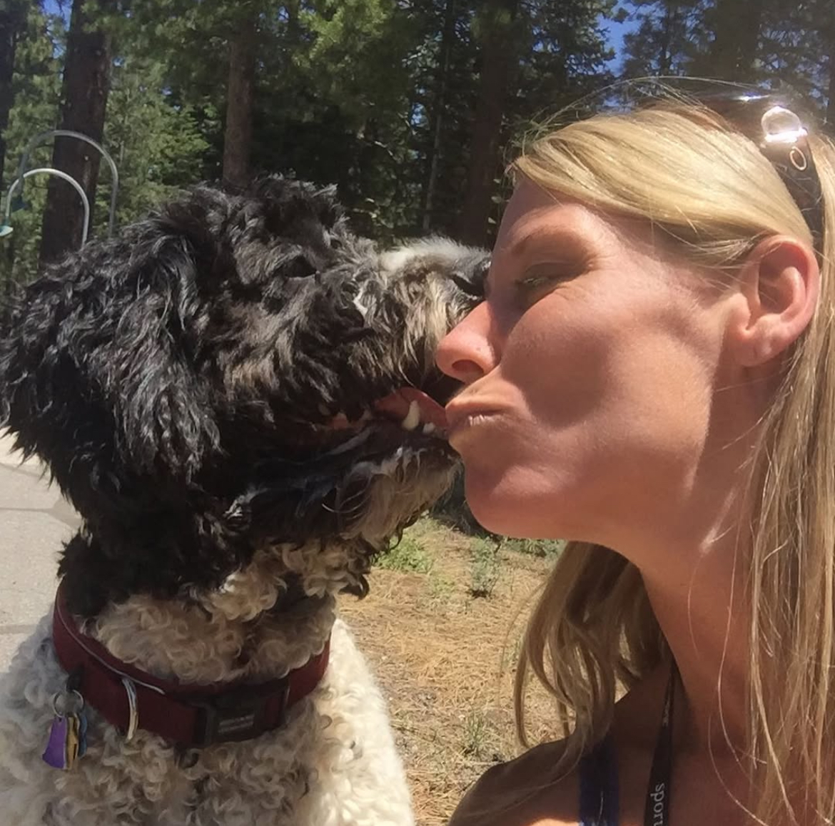 Southern California Pet Sitting . Woman kissing a curly black dog outdoors during pet sitting adventure.