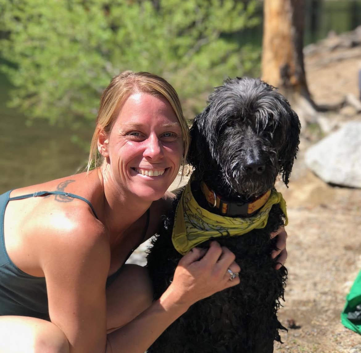 Woman hugging a large curly dog beside a peaceful stream.Southern California Pet Sitting 