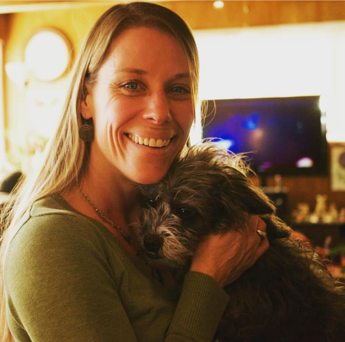 Southern California Pet Sitting . Blonde woman indoors holding a scruffy gray dog and smiling at the camera – Pet sitter embraces a scruffy pup in a cozy home setting, both radiating warmth and contentment.
