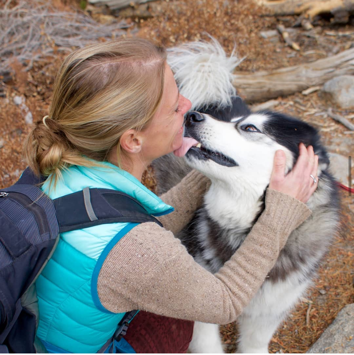 Blonde woman kissing a husky outdoors in autumn – Pet sitter shares a tender moment with a husky, surrounded by fall leaves and forest light. Southern California Pet Sitting 