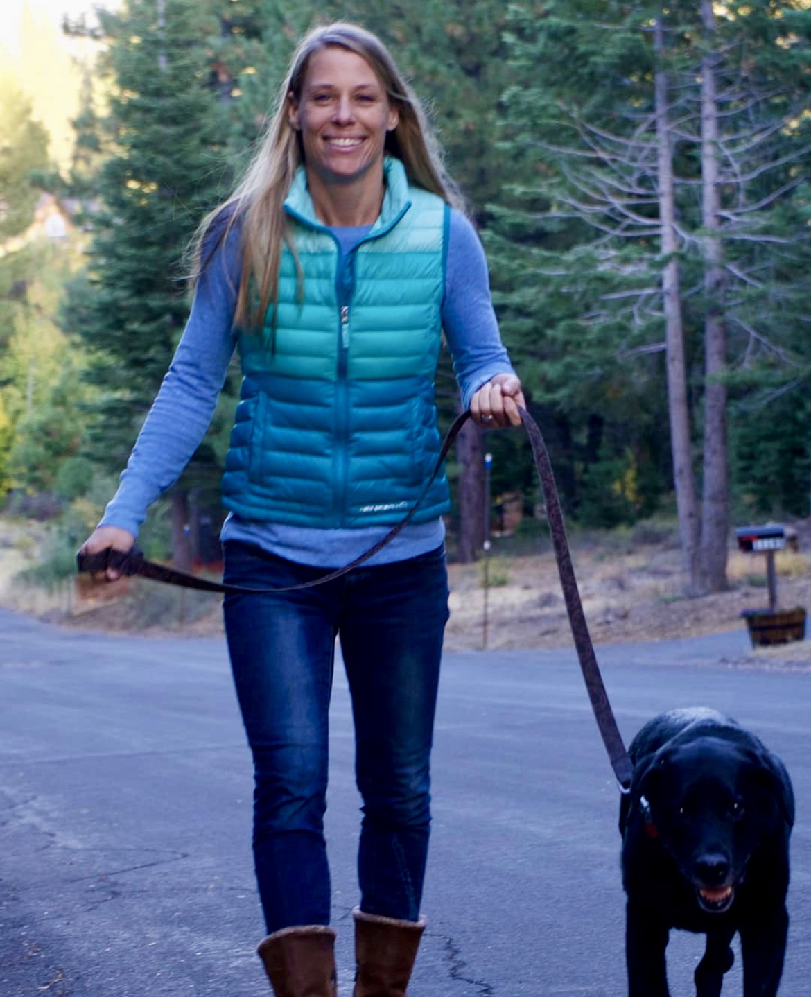 Aeray walks a black lab on the street in a forest neighborhood in Tahoe.  Southern California Pet Sitting 