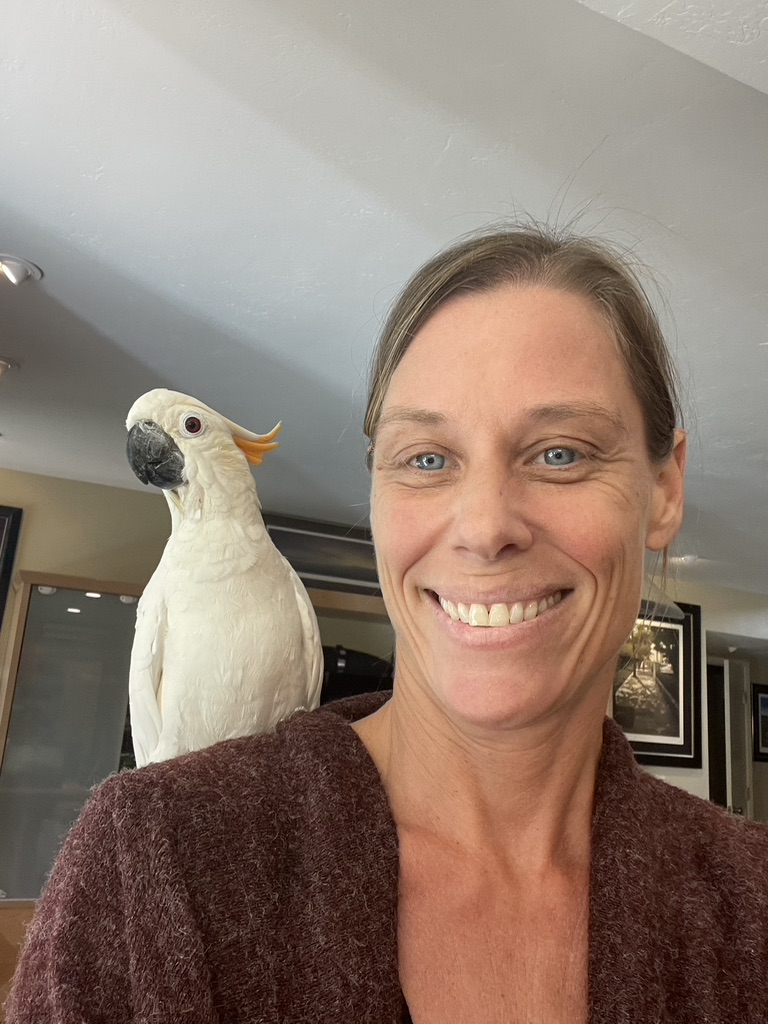 wonan with blond hair and. red sweater with a cockatoo on her shoulder. Southern California Pet Sitting 