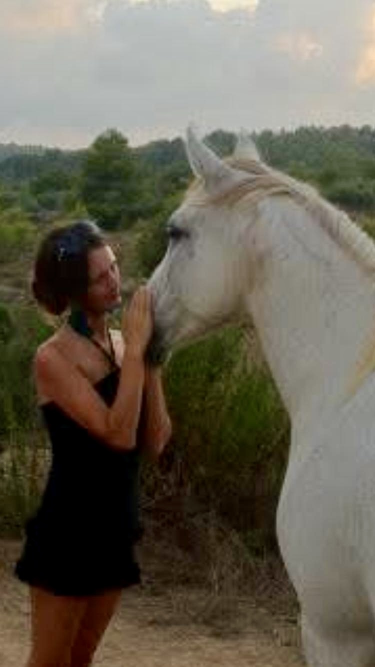Woman kissing a white horse on the nose in a green meadow – Deep connection between human and horse captured in a tender kiss amid lush greenery. Southern California Pet Sitting 