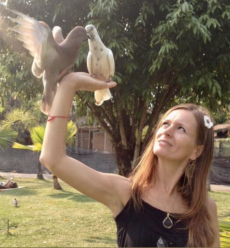Woman lifting two white doves with palms raised in a lush backyard – Magical moment with woman holding doves, symbolizing peace and connection with animals. Southern California Pet Sitting 