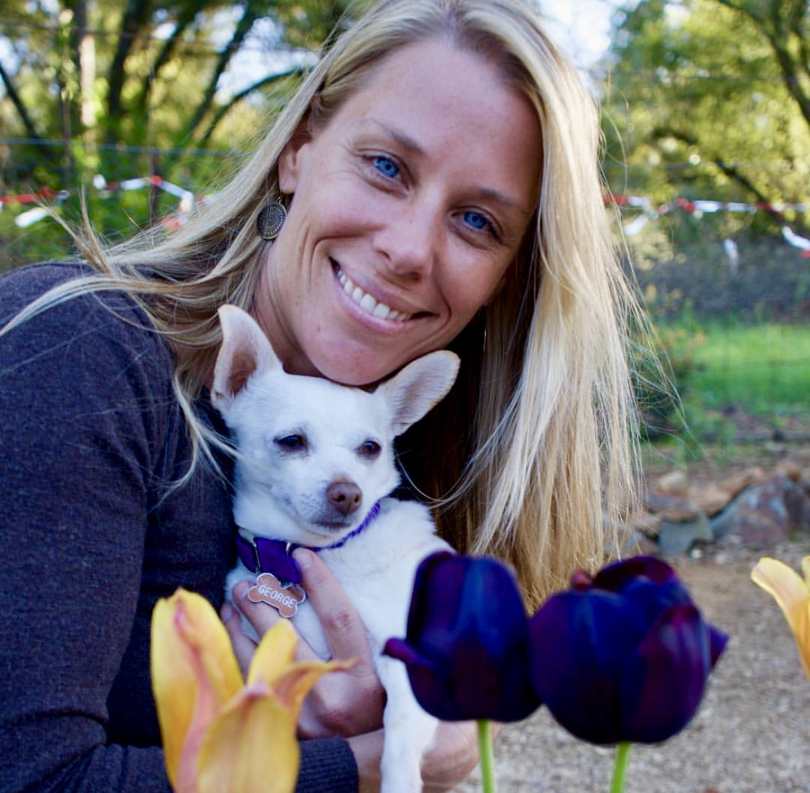 miling woman in a garden holding a white chihuahua, surrounded by spring tulips — peaceful moment with small dog in vibrant flowers. about Southern California Pet Sitting